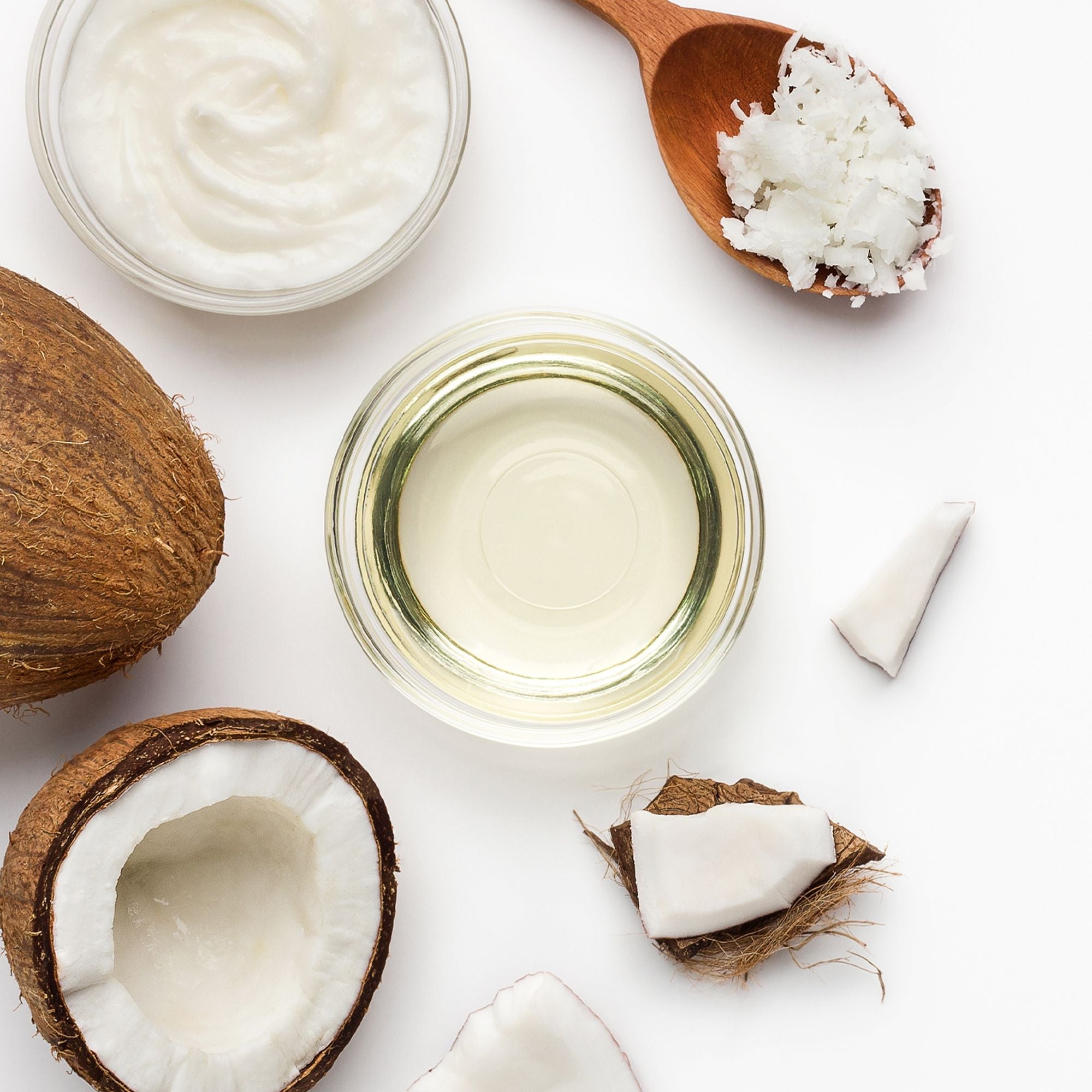 Olio di cocco, burro di cocco e pezzi di noce di cocco disposti su un piano bianco.